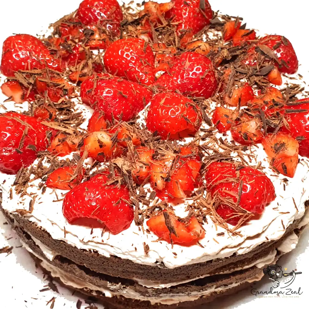 Three-layer almond flour chocolate cake topped with fresh strawberries and chocolate shavings