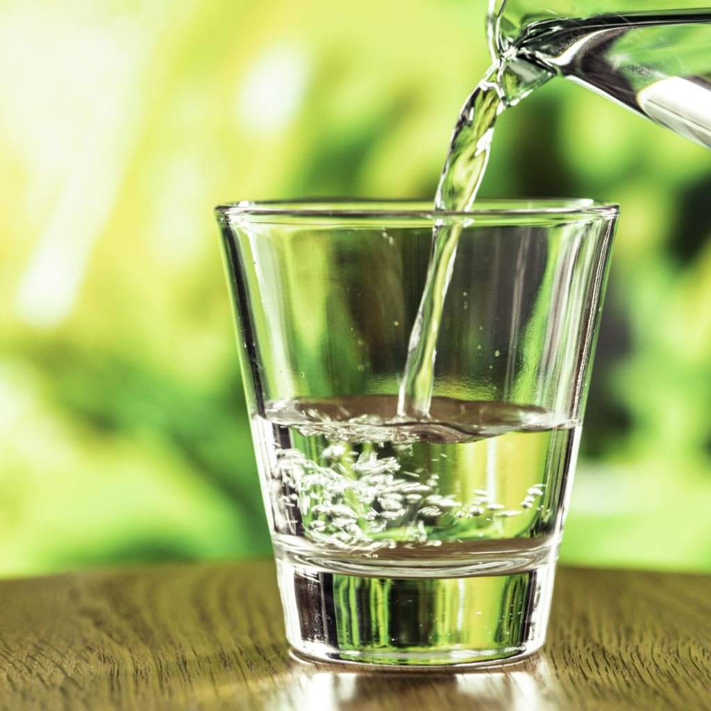 7 AMAZING HEALTH BENEFITS OF DRINKING WATER Close-up of water being poured from a jug into a glass on a wooden table — illustrating hydration and healthy habits