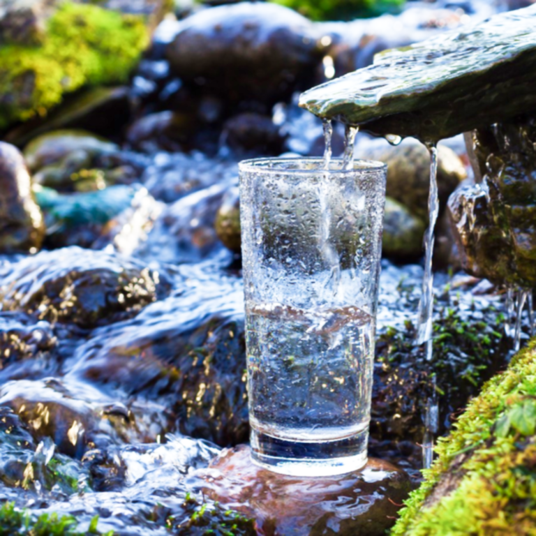 Glass of water placed in a rocky spring — featured image for a post about the health benefits of drinking water
