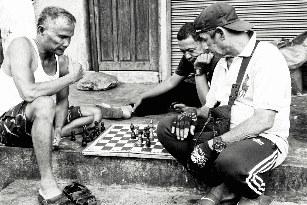 3 middle aged men playing chess on the steps in front a house