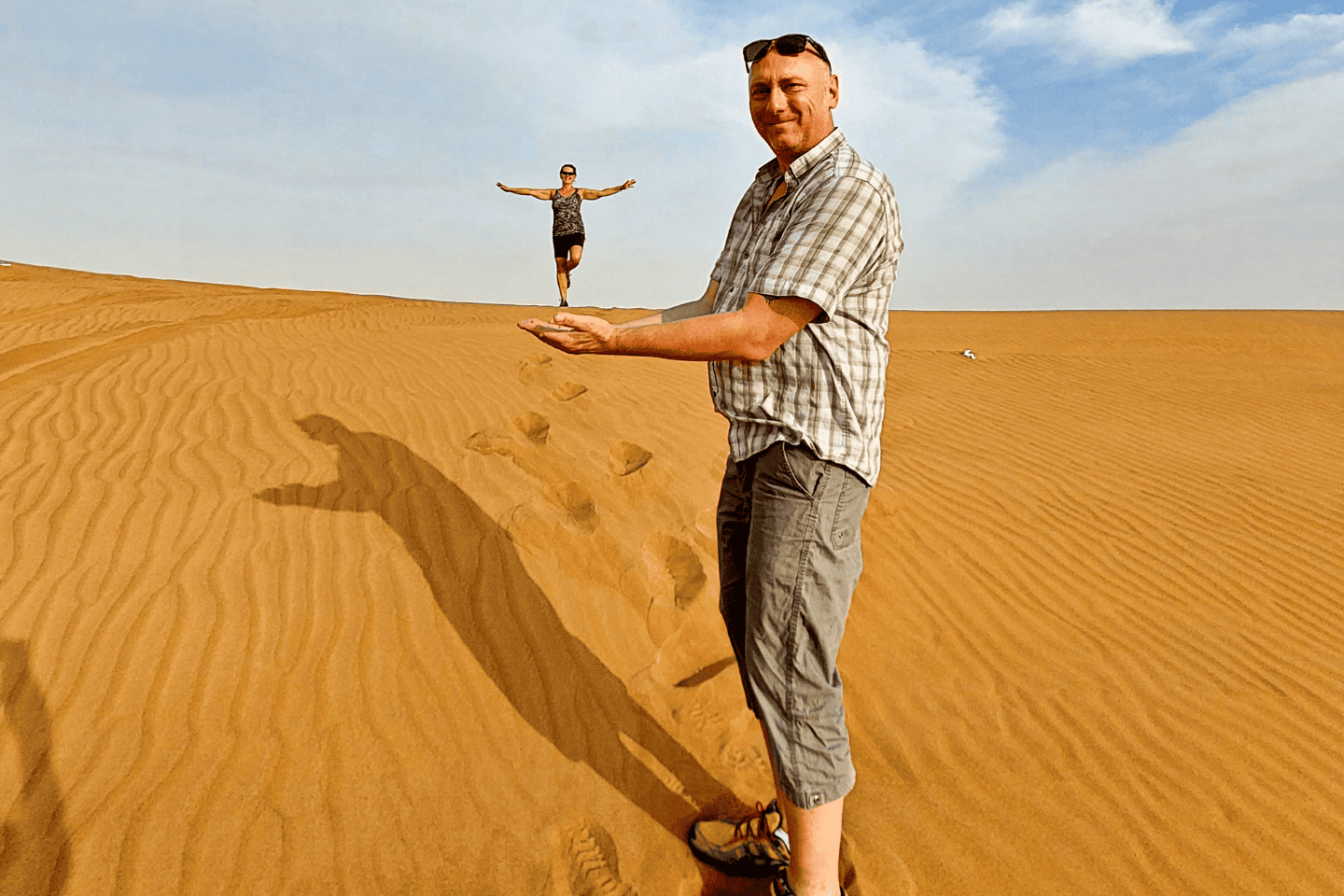 Playful perspective photo in the dunes ; Helena appears to stand in her husband's hands, reflecting the spirit of midlife relationship