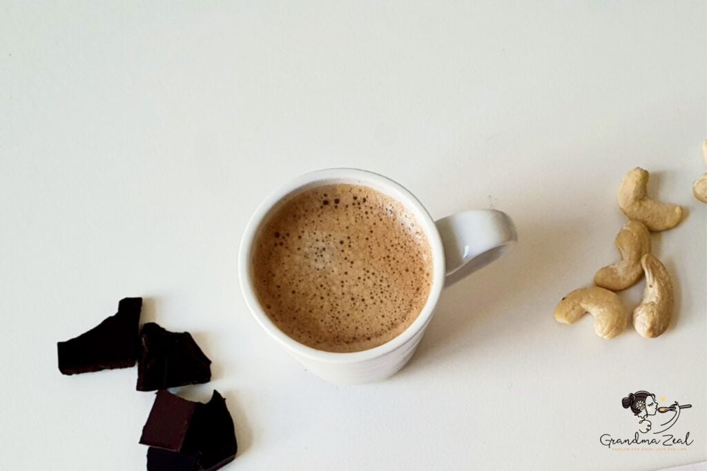 A cup of bulletproof coffee, cashew nuts and chocolate on the table