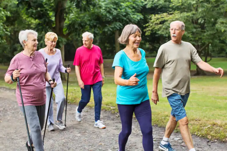 Middle-aged people walking in the park, some using Nordic walking sticks, showing how to age strong through regular movement and outdoor activity