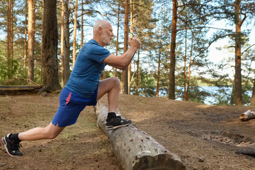 the man stretching outdoors with one leg on the fallen tree stump