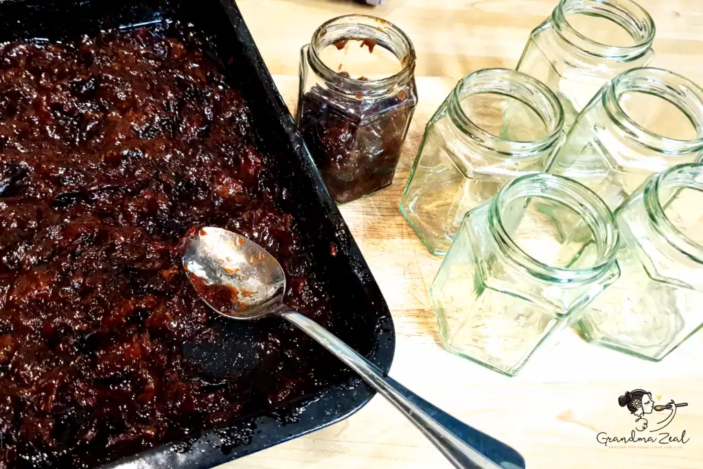 Sterilised jars  prepared for filling with dark, thick baked plum jam beside the baking tray after slow cooking