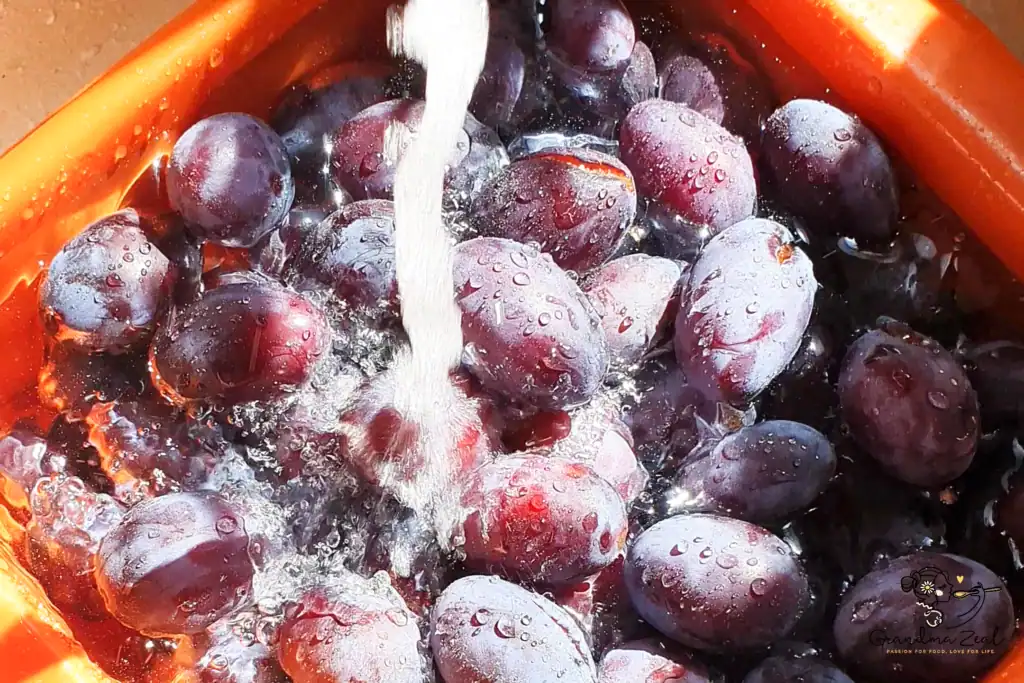 Whole plums being rinsed in a colander under running water, prepared for cooking