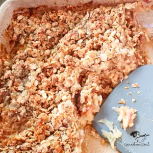 Healthy fruit crumble in baking dish with spatula, half served.