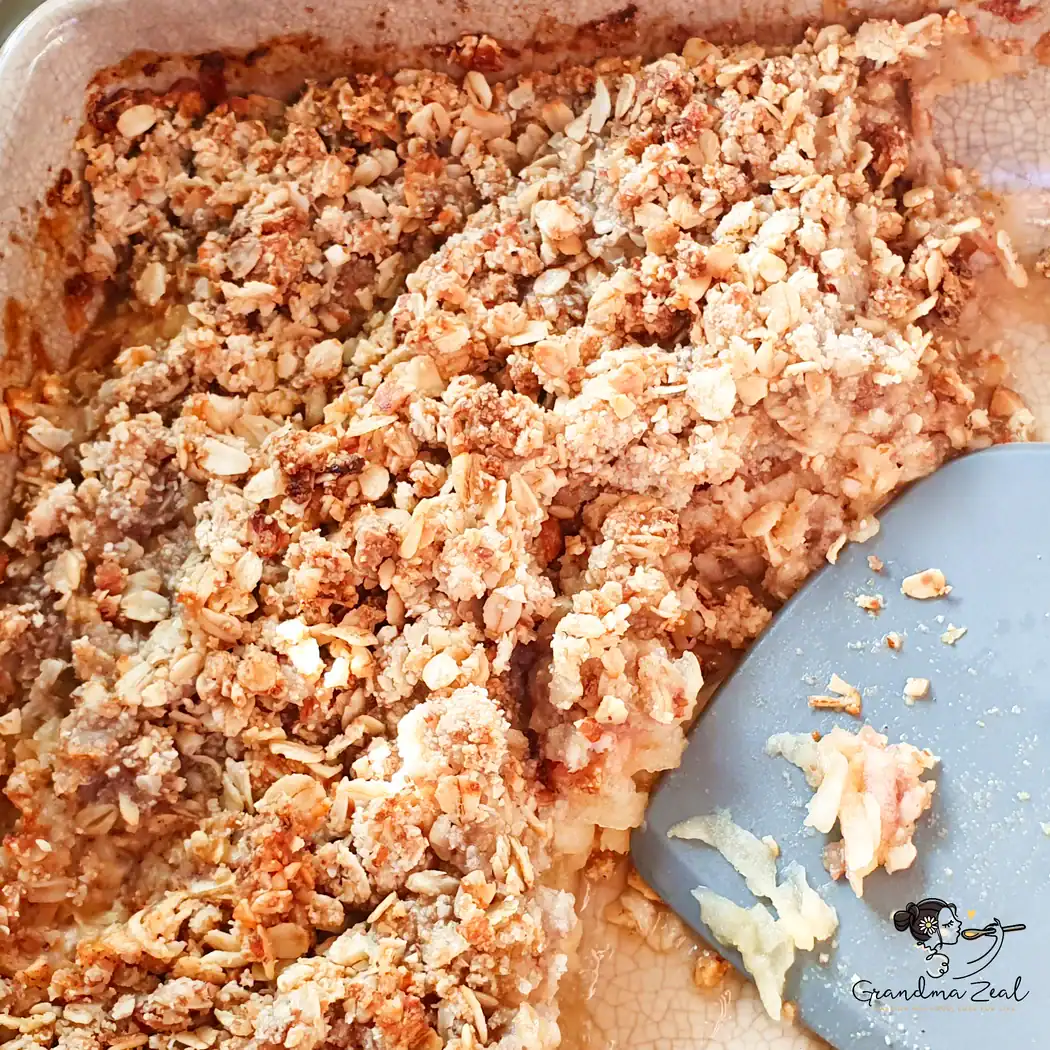 HEALTHY FRUIT CRUMBLE WITH APPLES, PEARS AND PLUMS Healthy fruit crumble in baking dish with spatula, half served.