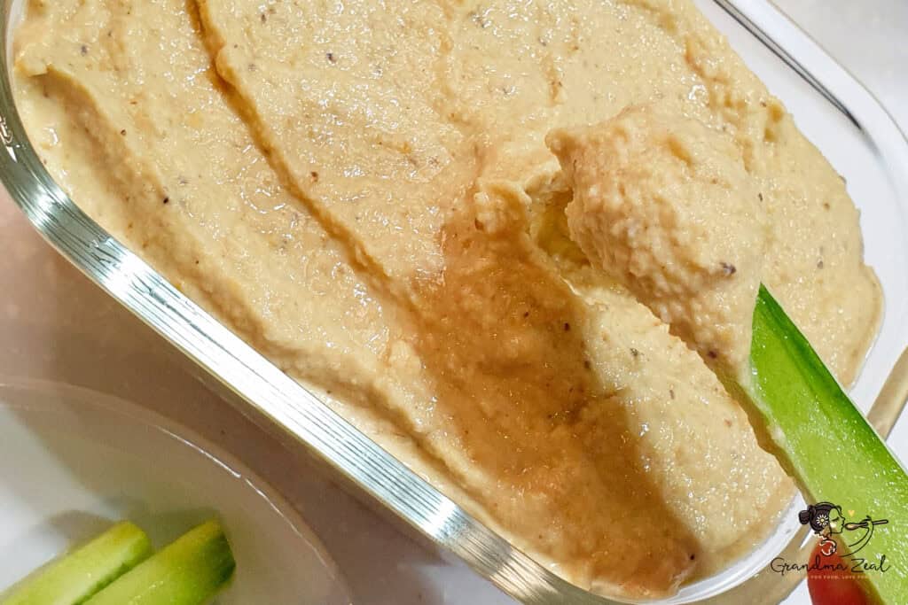 A close-up of creamy lentil humus being scooped with a fresh cucumber stick, showing the smooth texture 