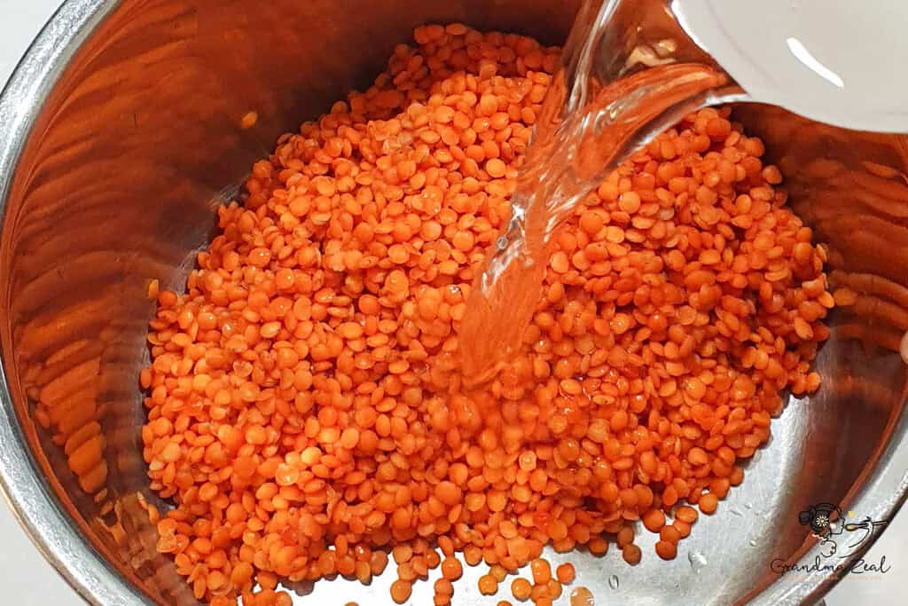pouring water into a saucepan filled with dry red lentils, ready to cook.