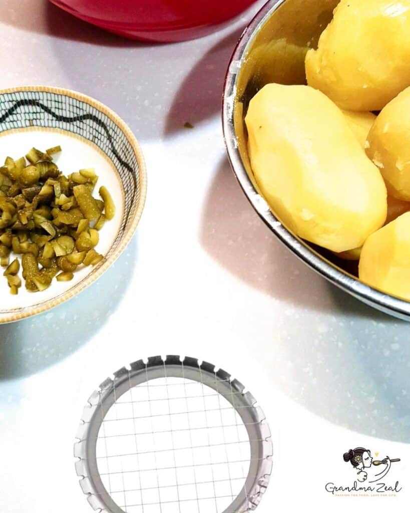 Peeled potatoes and chopped gherkins prepared for traditional homemade potato salad and the potato cutter