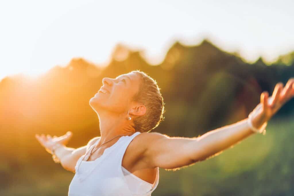 woman in the sunlight with opened arms and happy expression on the face