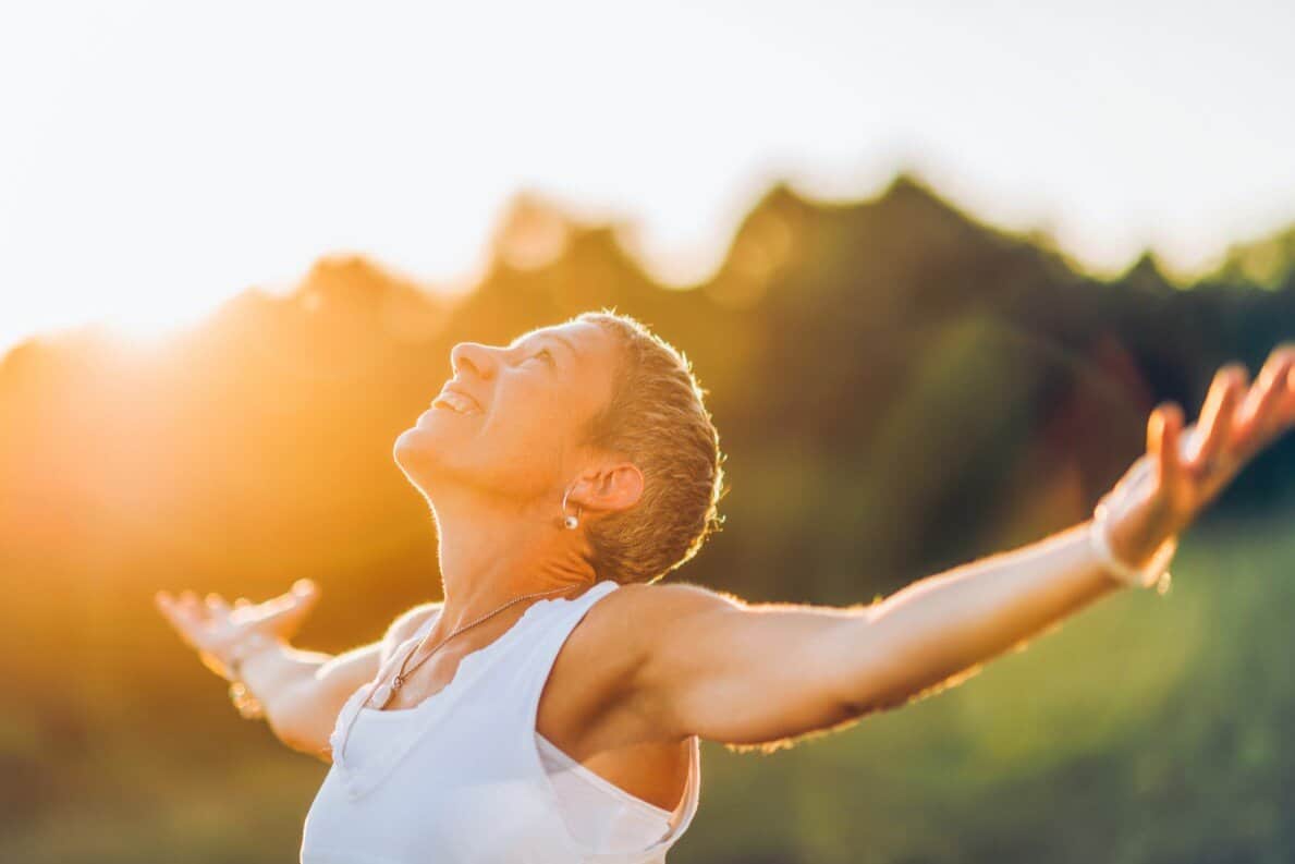 woman in the sunlight with opened arms and happy expression on the face