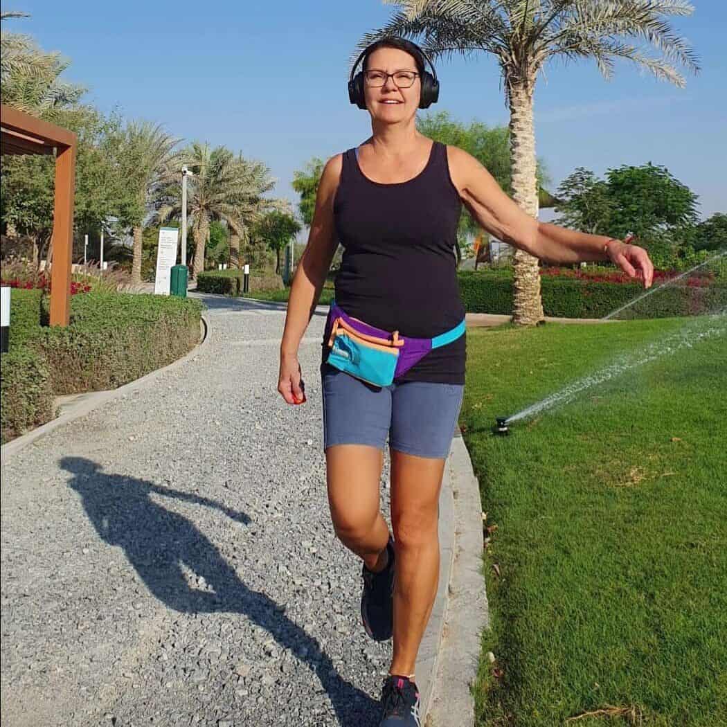 Helena walking outdoors on a sunny day, wearing headphones and sportswear.