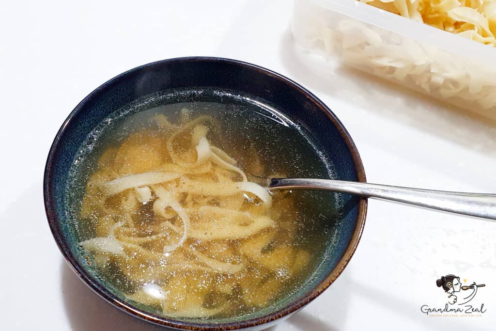 Clear chicken soup with handmade tagliatelle-style noodles in a ceramic bowl.
