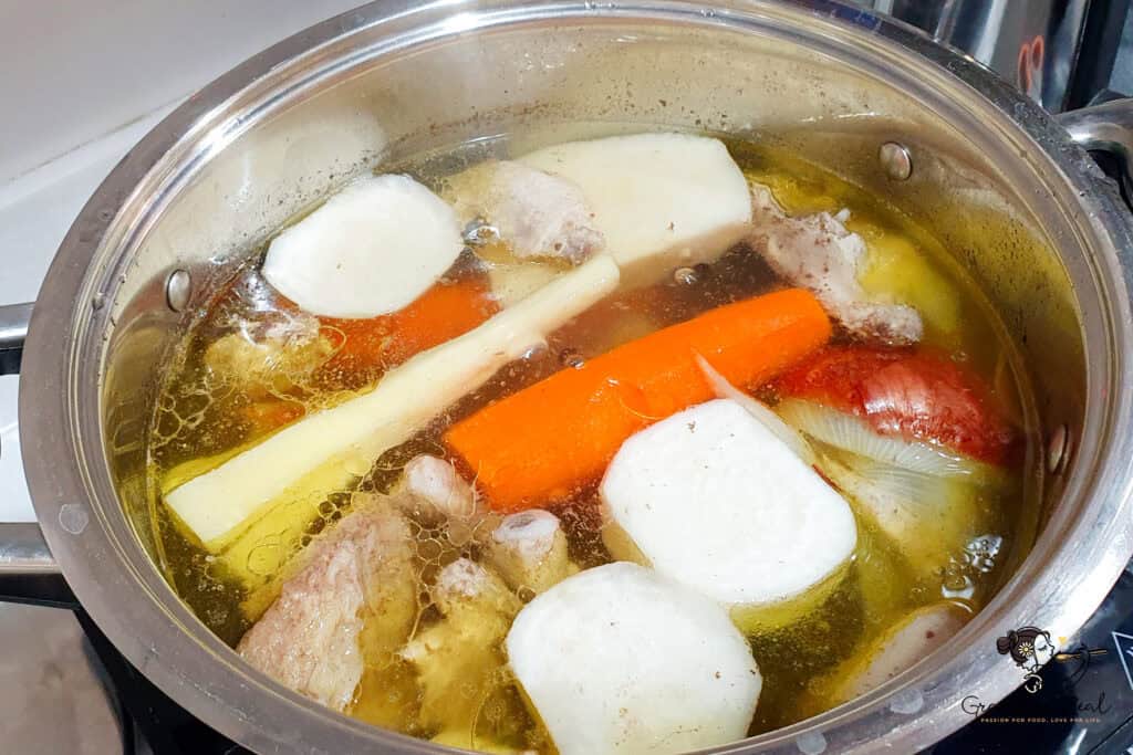 Homemade chicken soup cooking in a pot, with carrots, onion, root vegetables, and chicken pieces in golden broth.