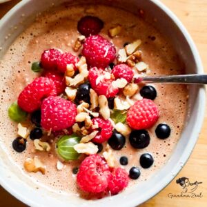 Overhead shot of a protein breakfast bowl topped with raspberries, blackcurrants, gooseberries, and chopped walnuts